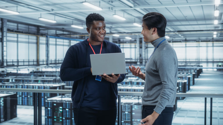 Computação na nuvem - imagem interna de um data center com um homem negro e um homem oriental com laptop em mãos conversando