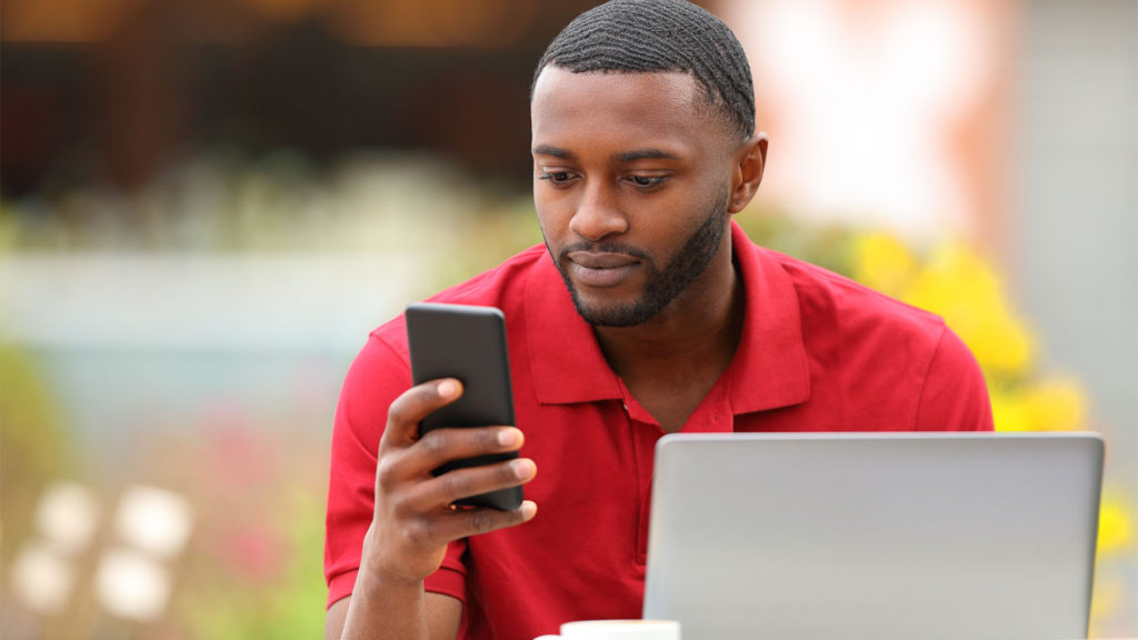Homem negro usando notebook e celular para conferir emails profissionais