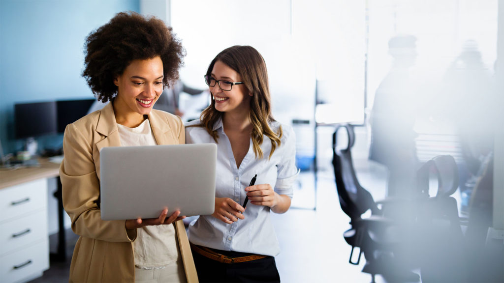 Duas mulheres sorrindo em frente ao notebook da empresa