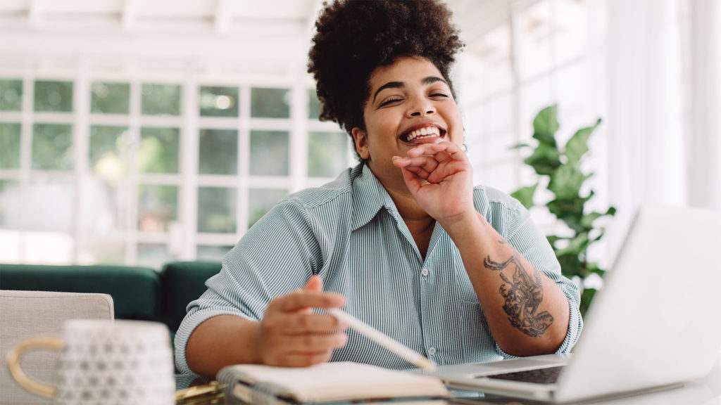 Mulher negra feliz em frente ao notebook, pois está trabalhando em uma rede segura.  