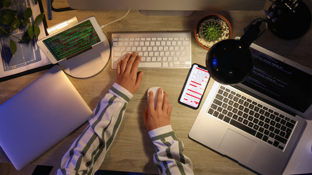 Um homem usando o teclado e um mouse com dois notebooks na mesa, um celular e um tablet
