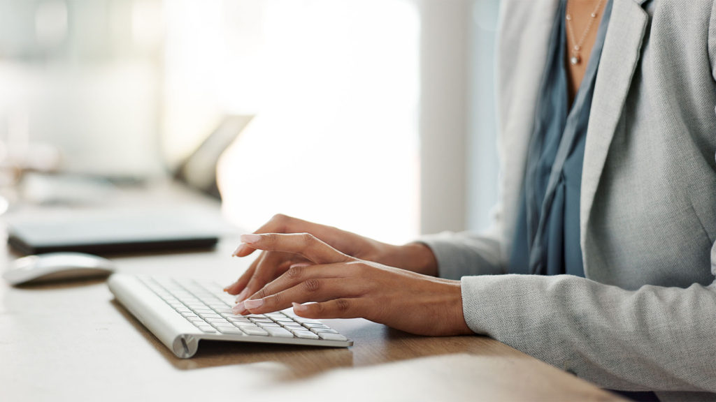 Mãos de uma mulher usando um teclado de computador. Leia mais sobre dicas para manter a segurança do seu e-mail corporativo