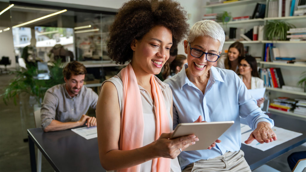 duas mulheres usando um tablet dentro de uma sala de reunião