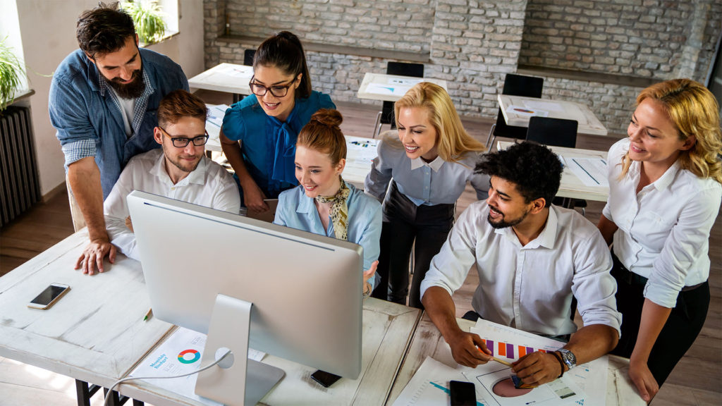 Equipe de trabalho composta por 4 homens e 3 mulheres em frente ao computador da empresa