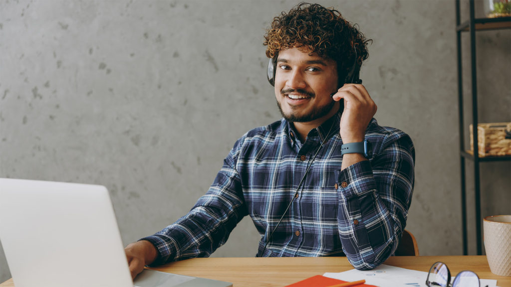 homem sorrindo usando um headset em frente ao notebook