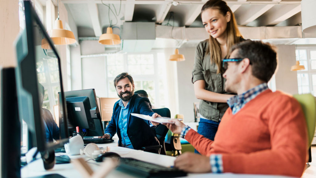 Dois homens e uma mulher sorrindo em frente ao computador com expressão tranquila, pois sabem como evitar a formação de silos de dados.