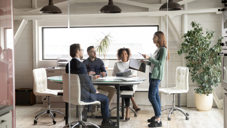 Três pessoas sentadas e um em pé numa reunião de empresa. Ao contratar uma terceirizada de TI você sabe a diferença entre SLA de solução x SLA de atendimento?