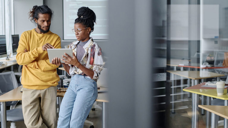 Um homem e uma mulher observando um tablet no emabiente de trabalho. Escalabilidade em TI traz mais flexibilidade para sua empresa continuar produzindo com excelência independentemente da demanda de trabalho