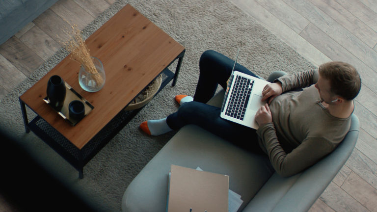 Home sentado com seu notebook no chão da sala. Como manter a segurança no trabalho híbrido?