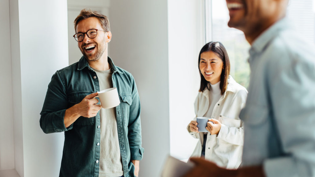 Dois homens e uma mulher sorrindo com canecas de café nas mãos, durante o trabalho. Faça sua automação de processos com a Dracones IT