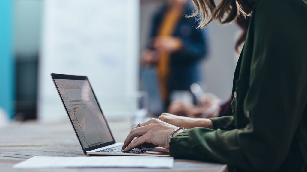 Uma mulher usando o notebook para escrever um texto. Saiba como a transformação digital nas empresas traz benefícios para qualquer negócio.