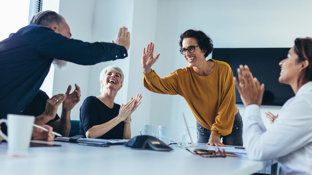 Três mulheres e três homens sentados em uma mesa de reunião felizes.